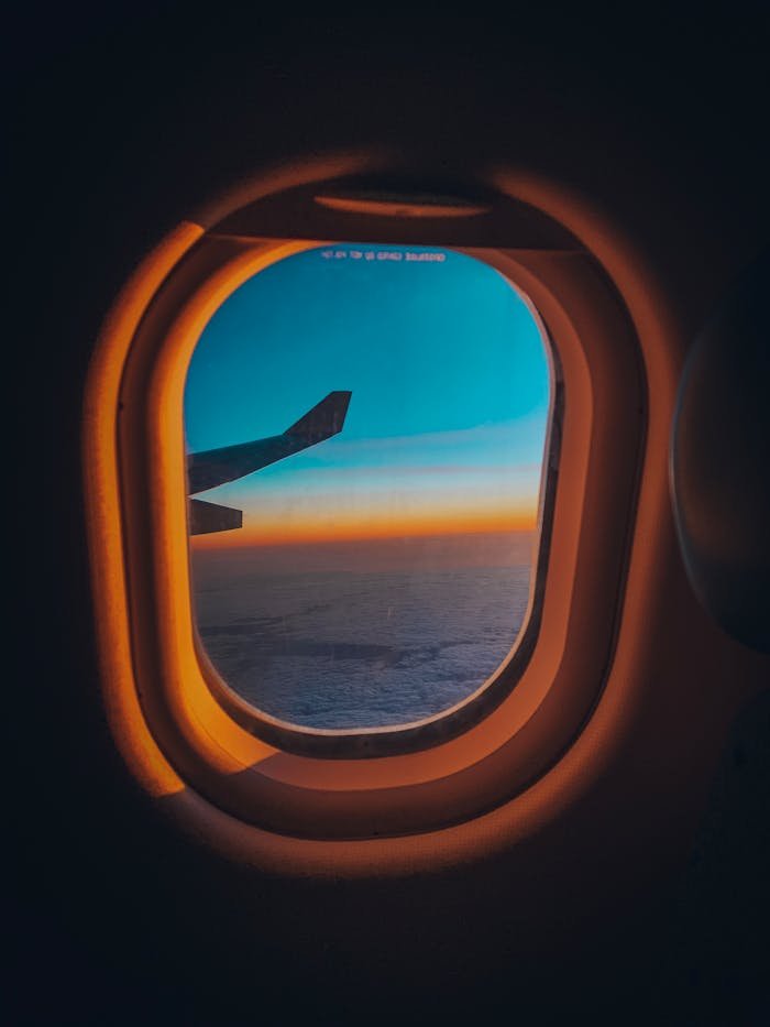 Experience the serene view from an airplane window overlooking a sunset sky and ocean horizon.